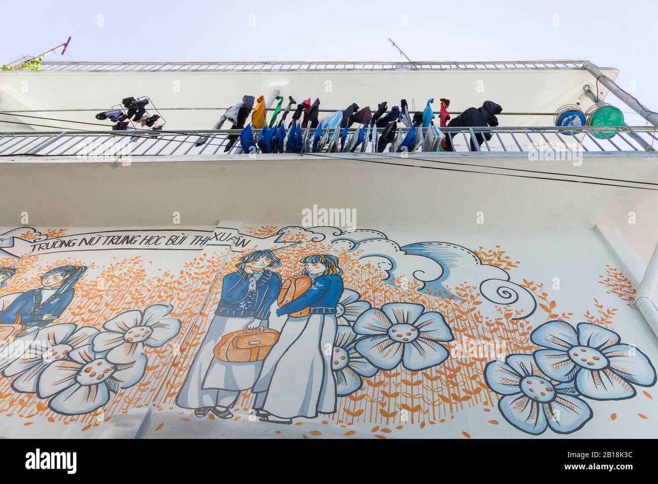 Affresco di studentesse in ao dai per la scuola superiore femminile Bui Thi Xuan sotto il bucato che asciuga su un balcone, Da Lat, Vietnam. Foto Stock