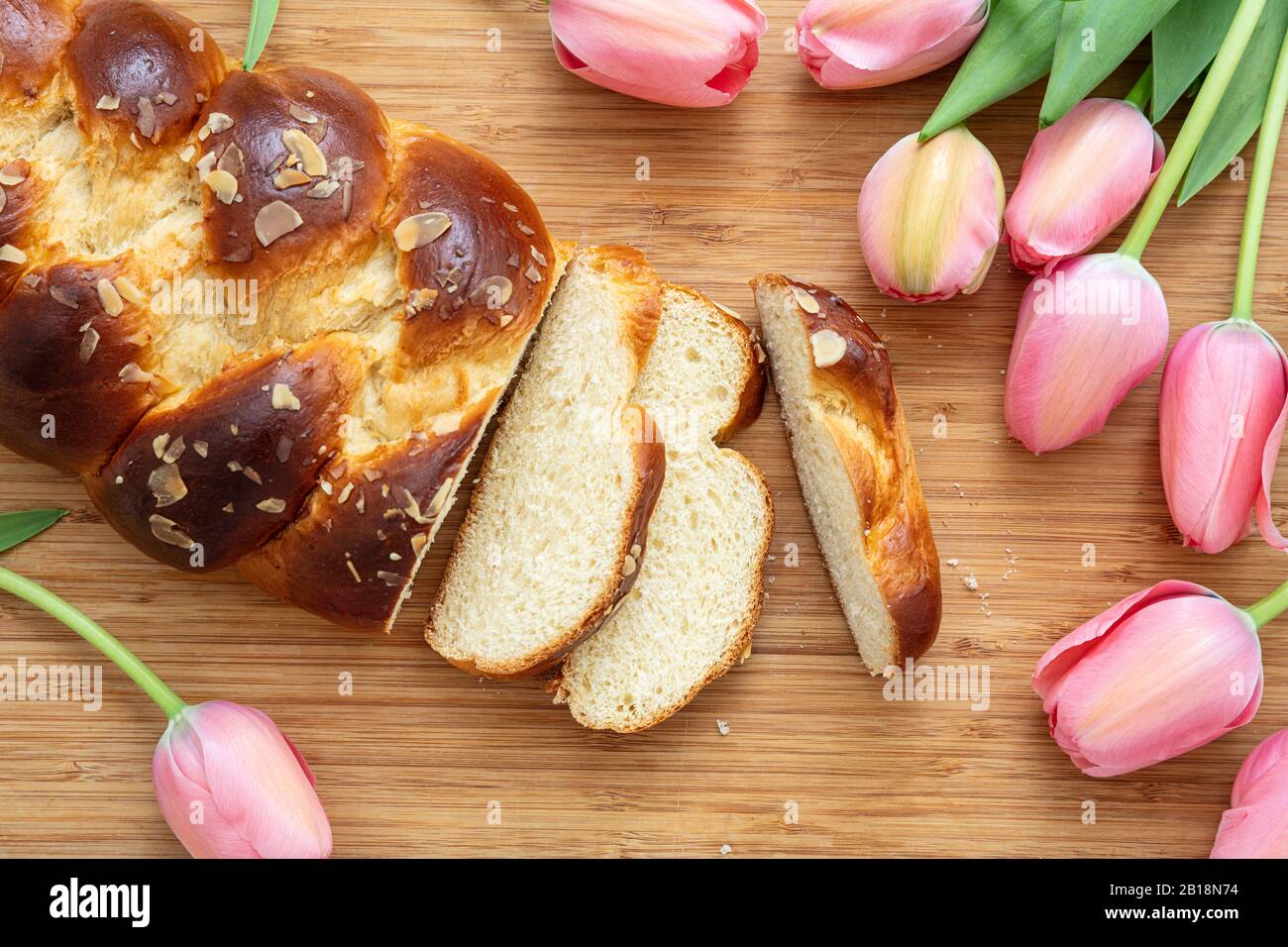 Pane dolce di Pasqua, tsoureki coconac affettato su sfondo tavola di legno, decorazione tulipani rosa, vista dall'alto. Tempo di Pasqua, primavera Foto Stock