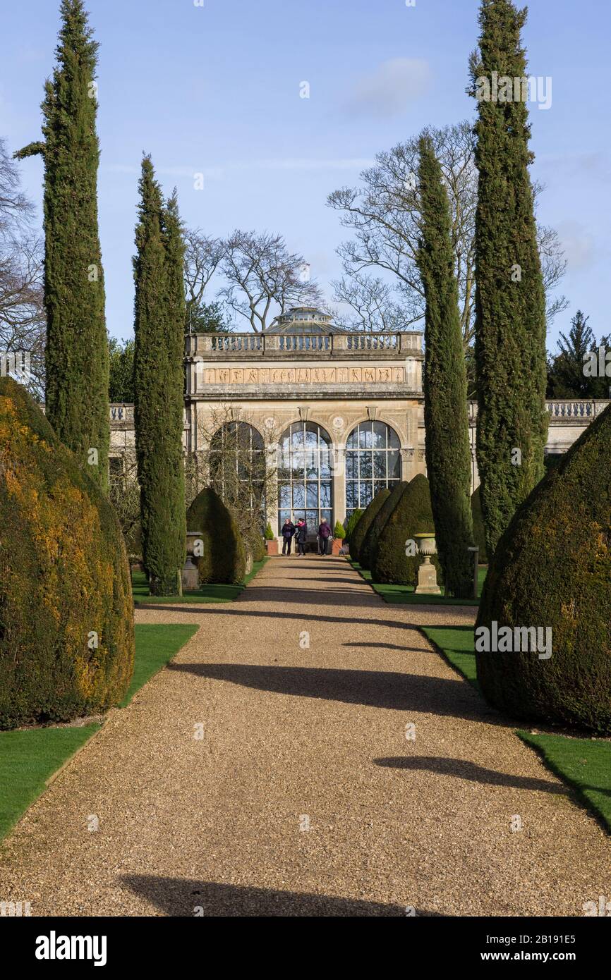 Sentiero di ghiaia che conduce, tra cespugli sempreverdi e alberi, all'Orangerie del 19th secolo; Castle Ashby Gardens, Northamptonshire, Regno Unito Foto Stock