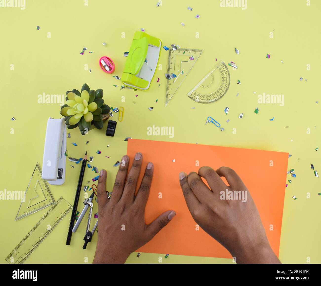 Diversi materiali di studio sparsi su uno sfondo di carta gialla mentre una persona sta disegnando su una carta arancione con una bussola Foto Stock