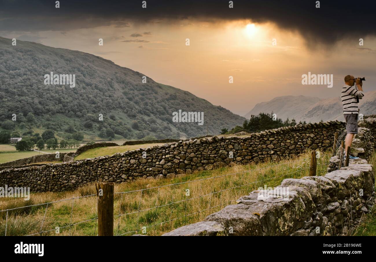 Fotografo di viaggio in piedi su muraglia di pietra asciutta che spara il Passo di Kirkstone, il Parco Nazionale del Distretto dei Laghi, Cumbria, Inghilterra Foto Stock