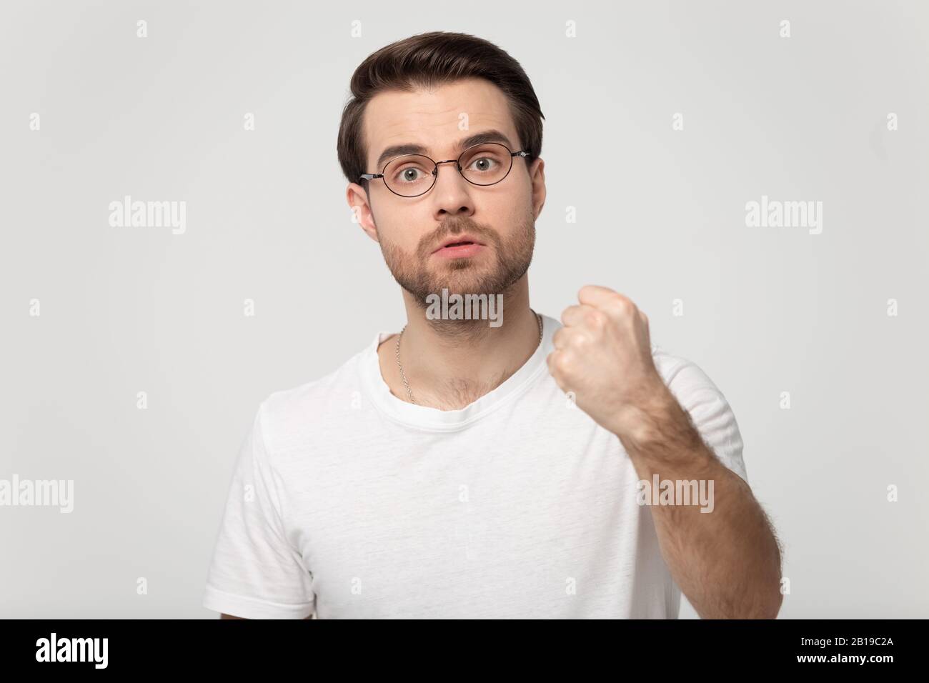 Giovane uomo aggressivo in occhiali clenching pugno, dimostrando il potere. Foto Stock