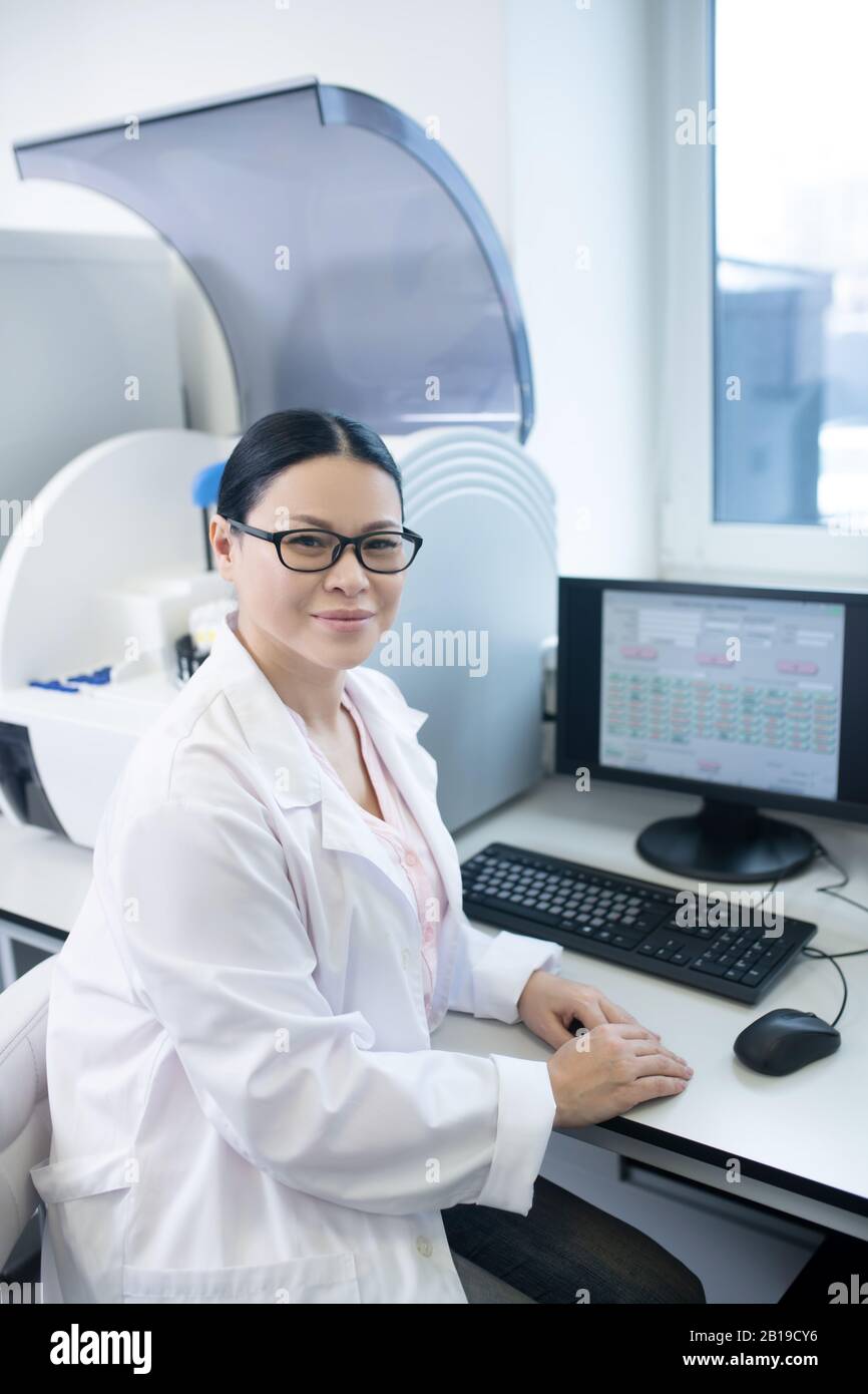 Medico dai capelli scuri in un accappatoio bianco che lavora su un computer Foto Stock
