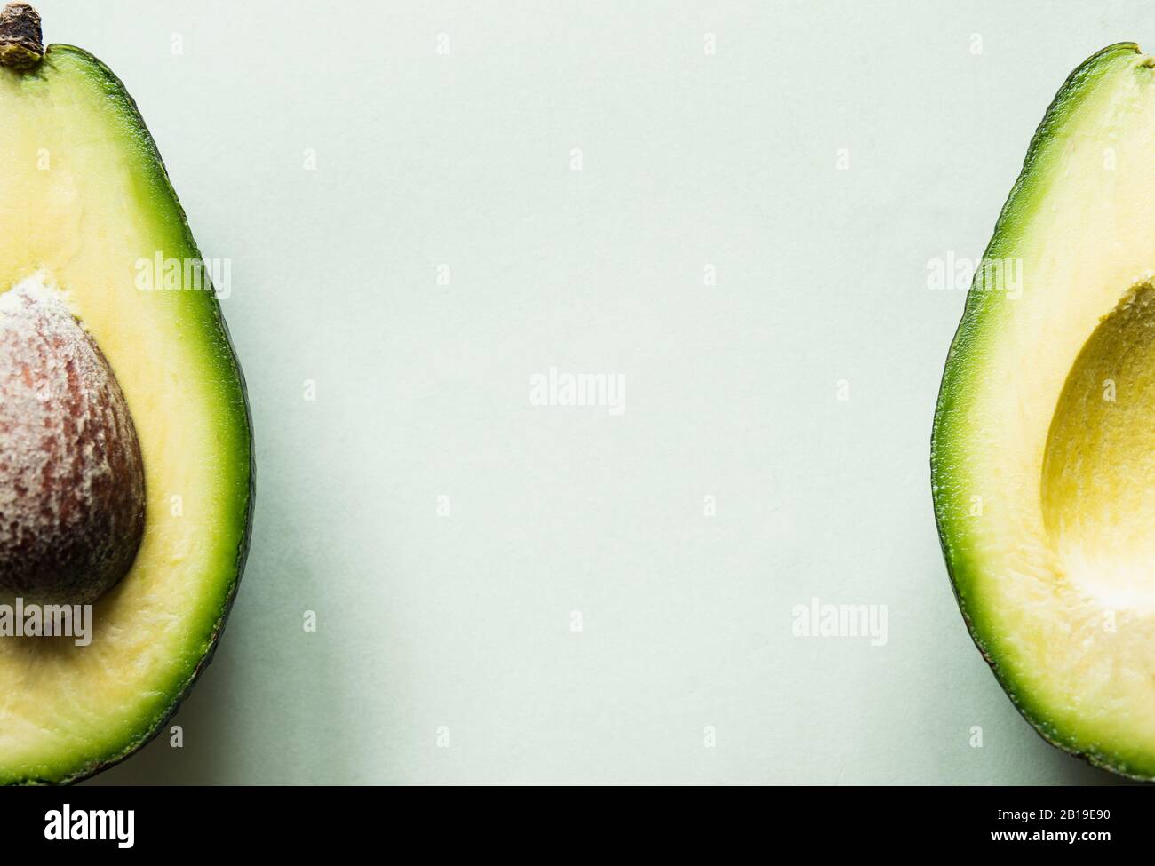 Pronto a mangiare avocado tagliato in due metà, isolato su sfondo verde chiaro. Foto Stock