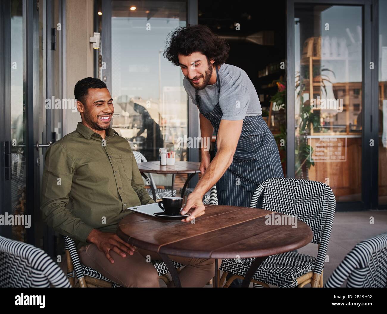 Allegro giovane uomo che serve un cliente afro-americano alla caffetteria Foto Stock