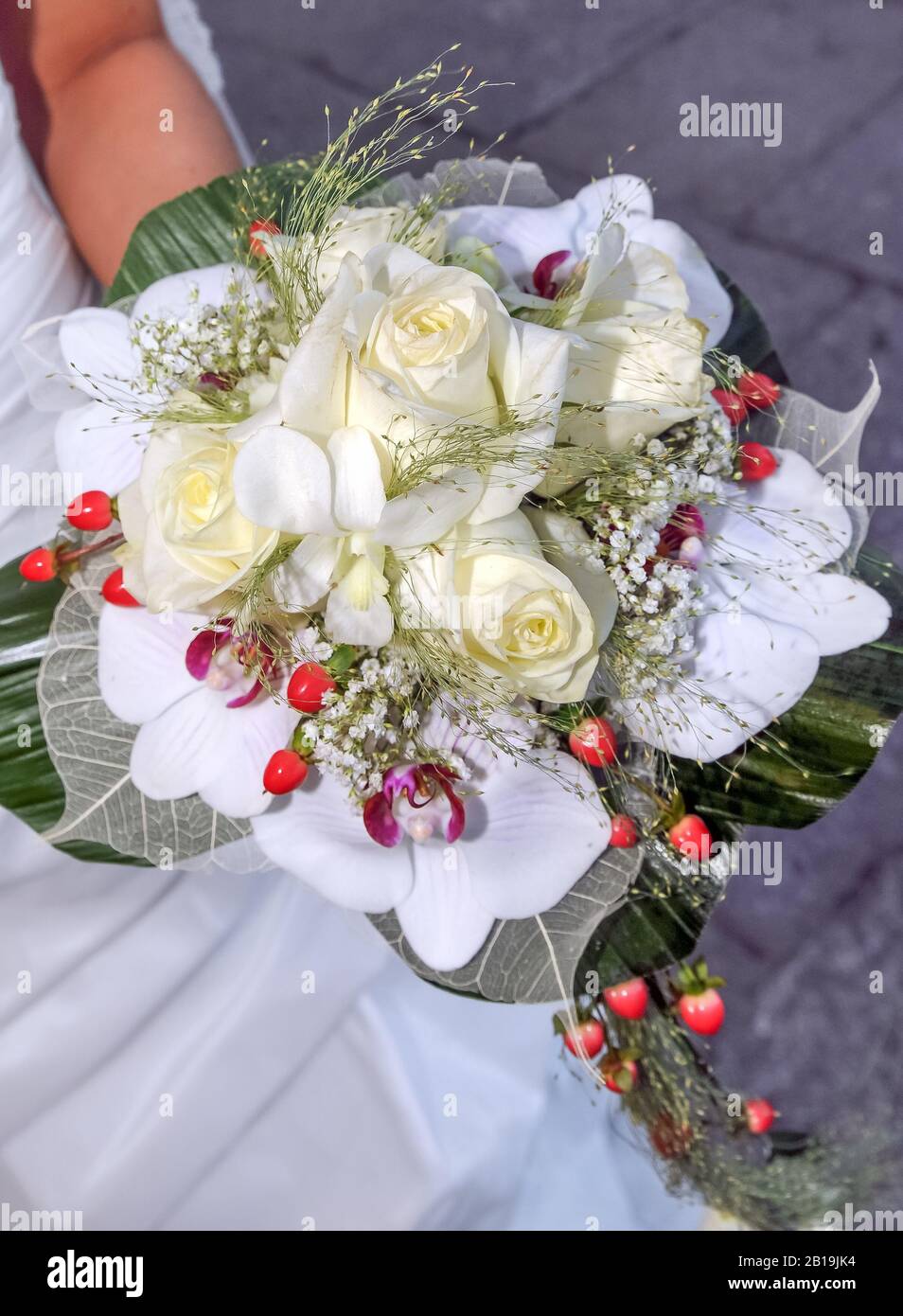 Bel bouquet di rose bianche con orchidee e bacche rosse tenuto dalla mano  di una sposa il suo giorno di nozze. Roses, Orchidelle Foto stock - Alamy