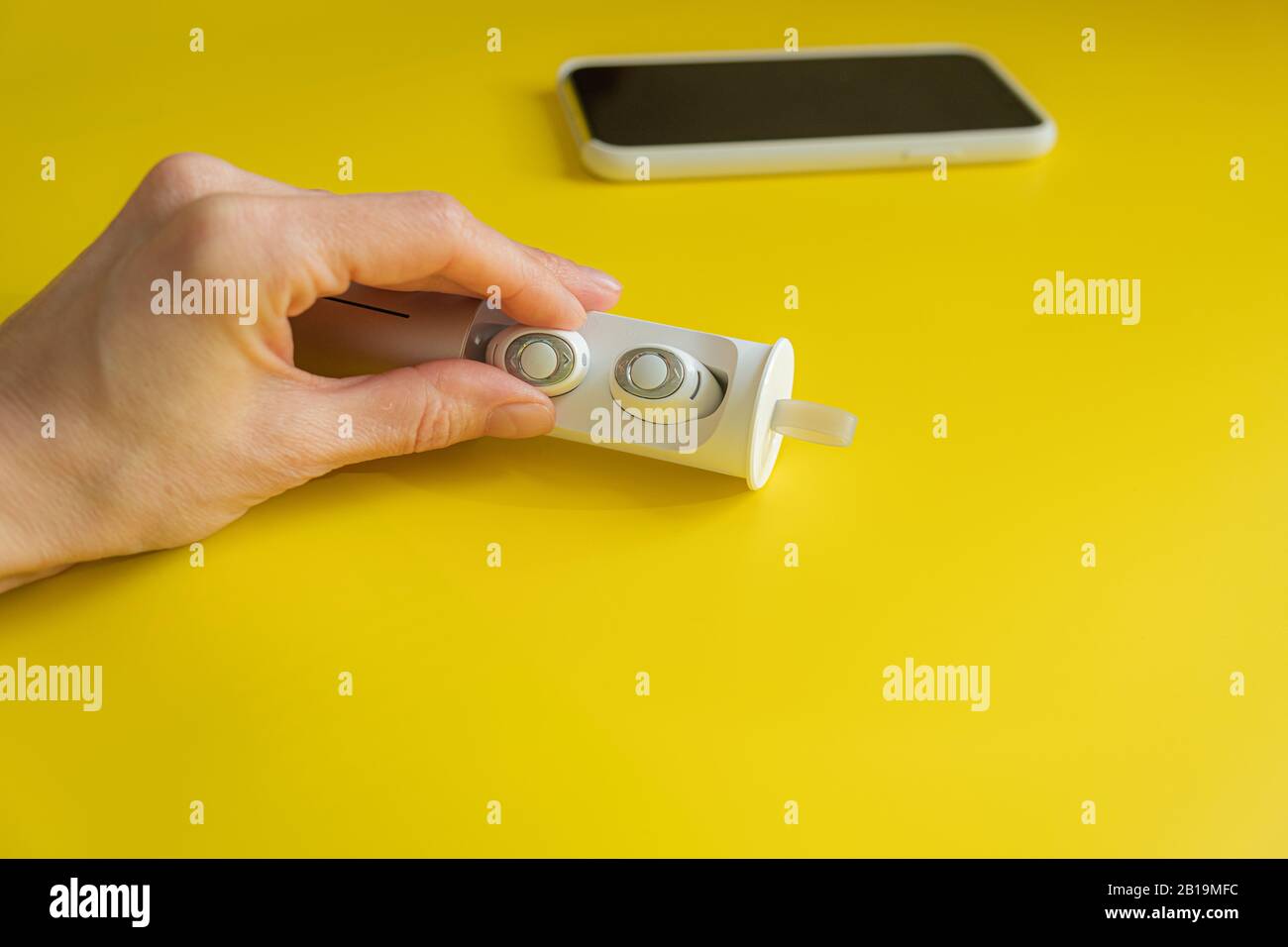 Cuffie wireless bianche per smartphone su sfondo giallo brillante, concetto di minimalismo Foto Stock