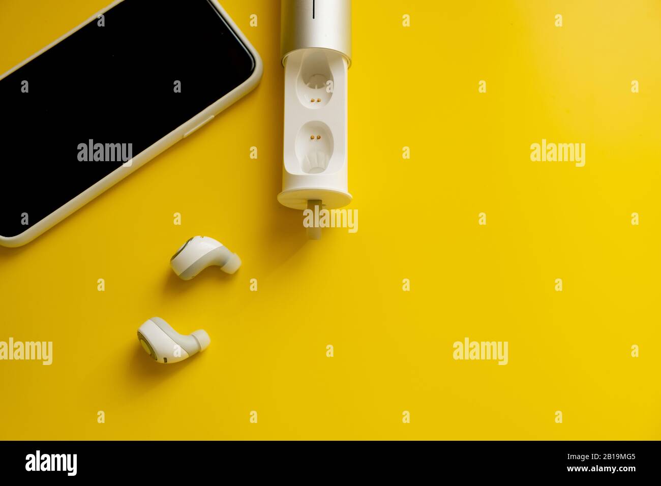 Cuffie wireless bianche per smartphone su sfondo giallo brillante, concetto di minimalismo Foto Stock
