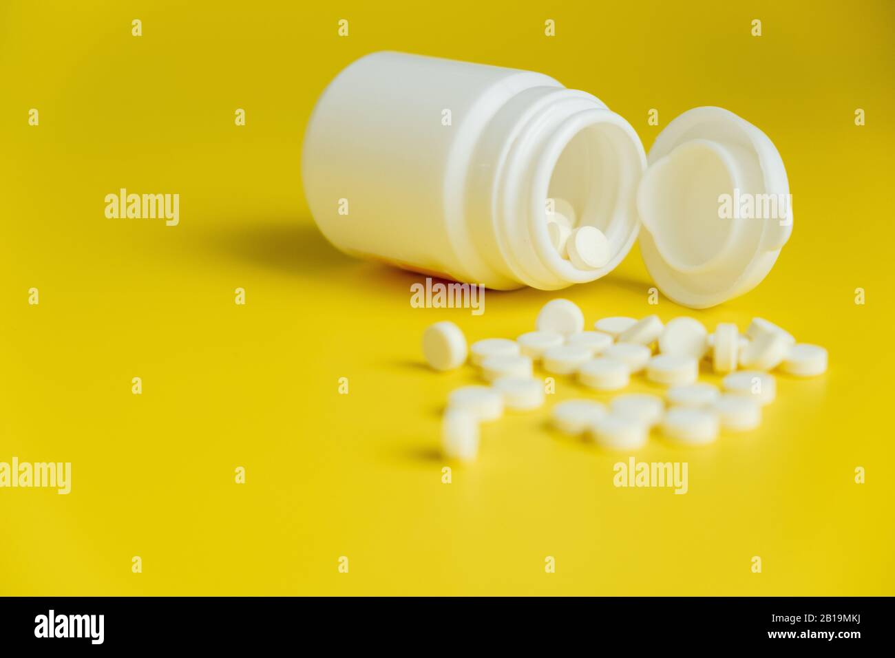 Pillole bianche e bottiglia bianca su uno sfondo giallo brillante, sano e concetto di medicina. Minimalismo. Spazio di copia Foto Stock