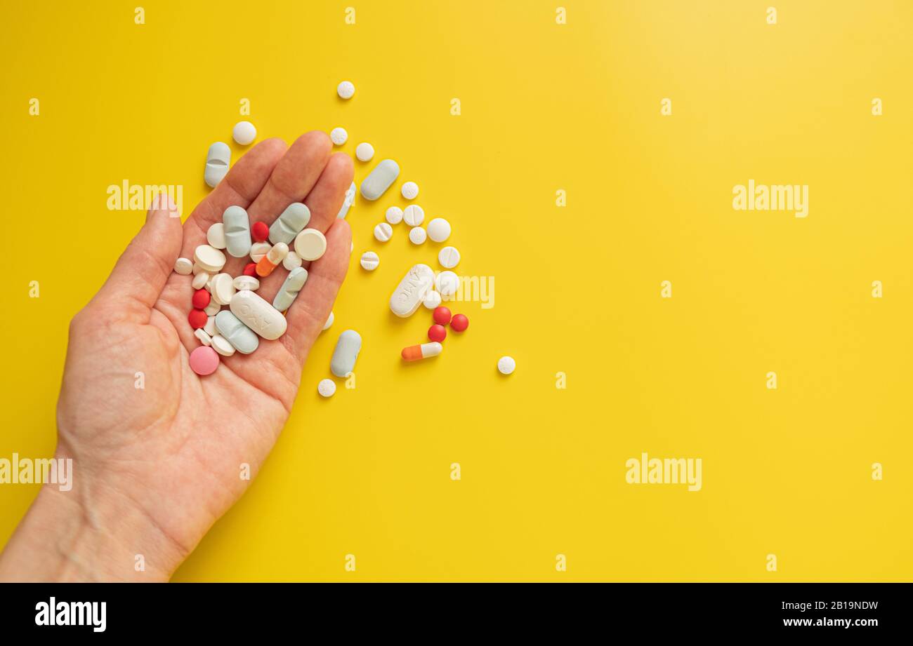 Molte compresse diverse pillole in mano di una donna su uno sfondo giallo brillante. Concetto di salute e medicina, copia spazio Foto Stock