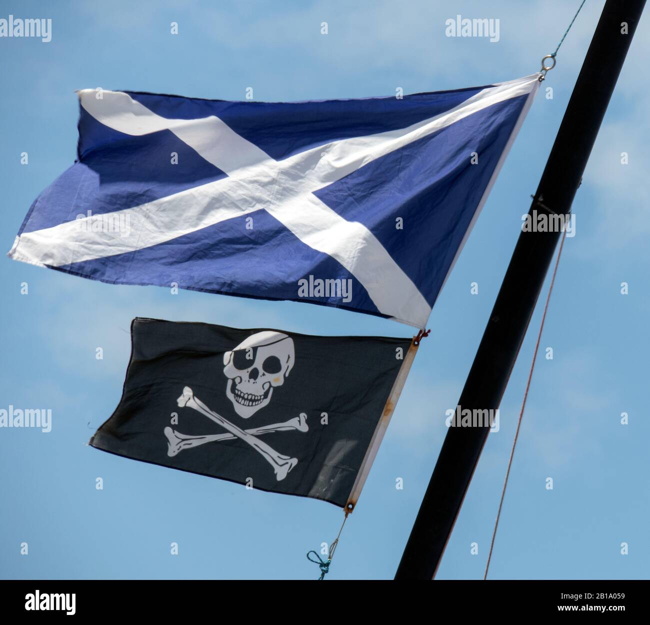 Navi Mast su Tresaith Beach che mostra il vento soffiato bandiera nazionale scozzese e il cranio e le ossa incrociate o noto come la bandiera Jolly Roger Foto Stock