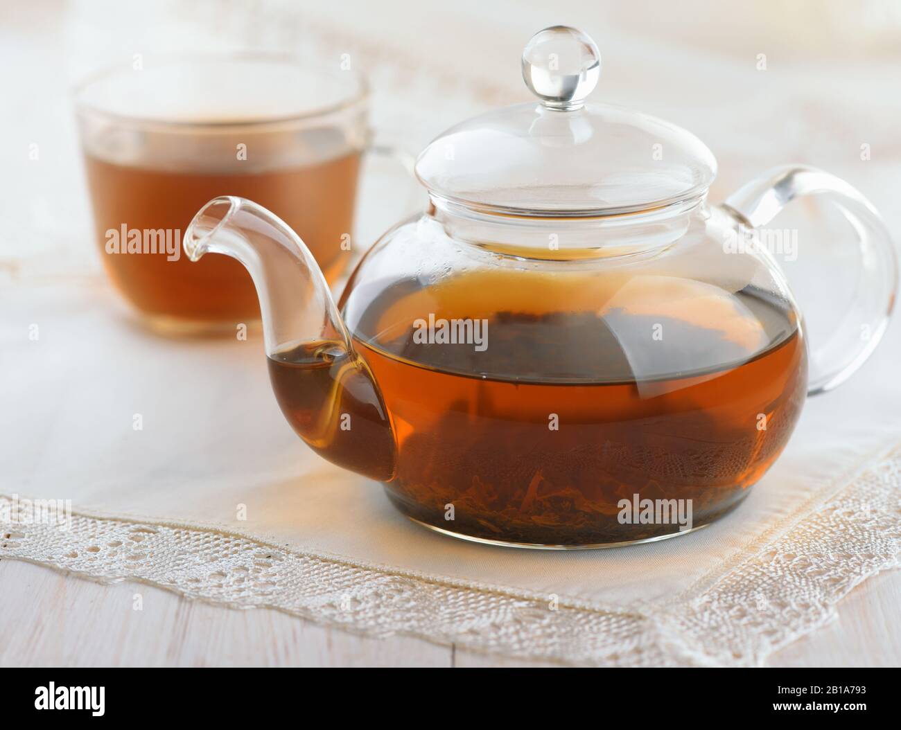 Teiera di vetro e tazza piena di tè nero fresco su tavolo di legno bianco Foto Stock
