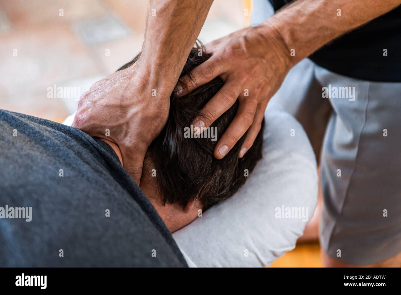 Un giovane uomo sul trattamento benessere massaggio sportivo. Un massaggiatore sportivo maschile che effettua massaggio alla testa e al collo. Uno sportivo che gode di un massaggio Foto Stock