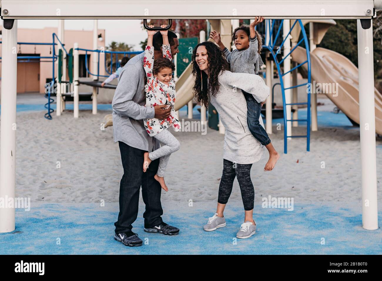 Una famiglia felice che gioca all'aperto al parco giochi al tramonto Foto Stock