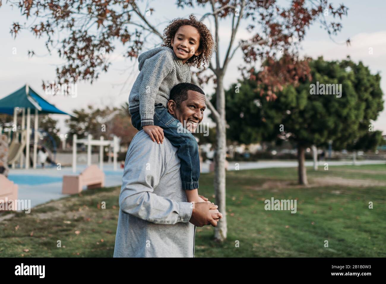 Ragazzo carino seduto sulle spalle di un padre felice al parco giochi Foto Stock