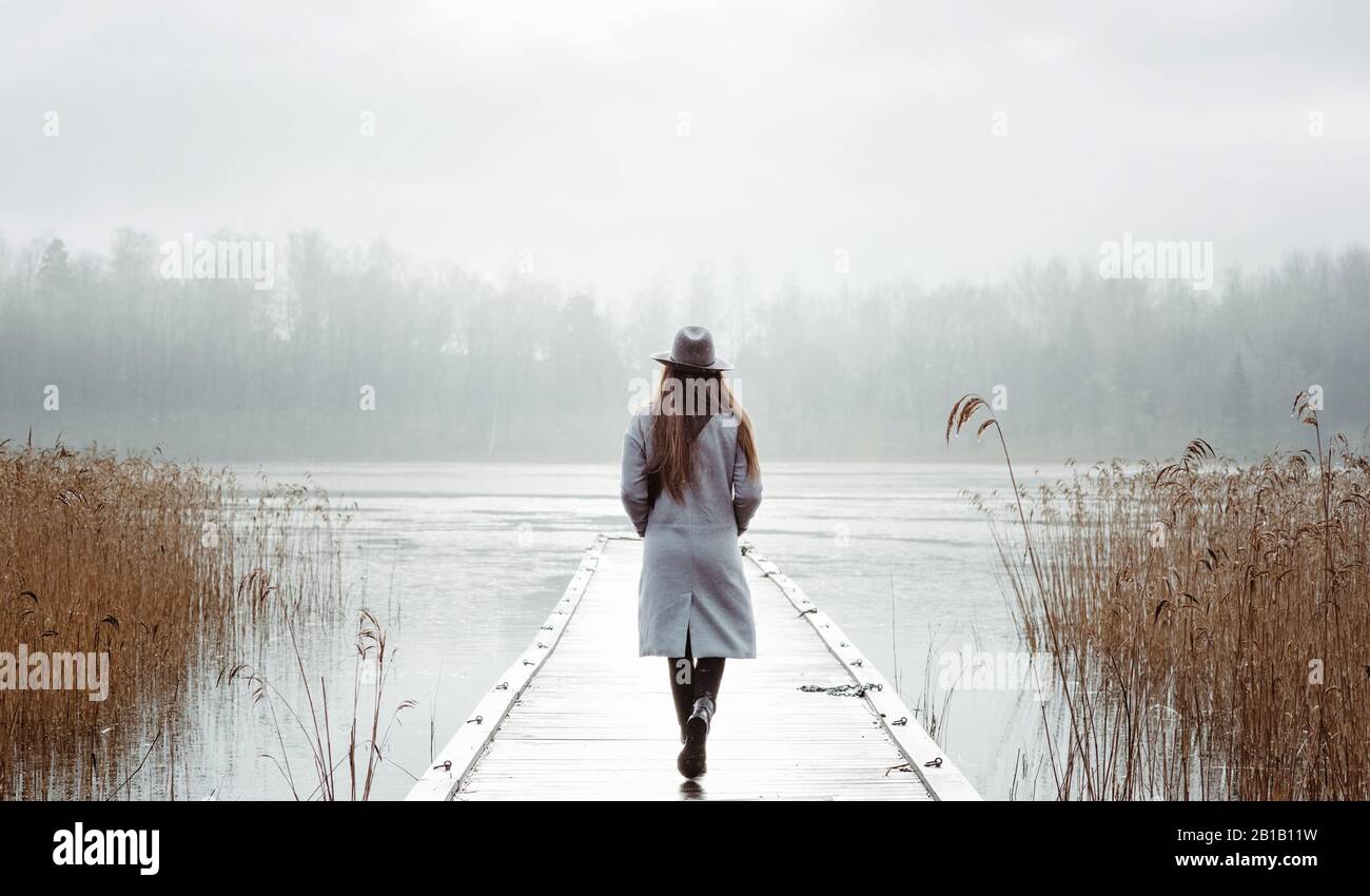 donna che cammina da sola pensando al mare in inverno su un molo Foto Stock
