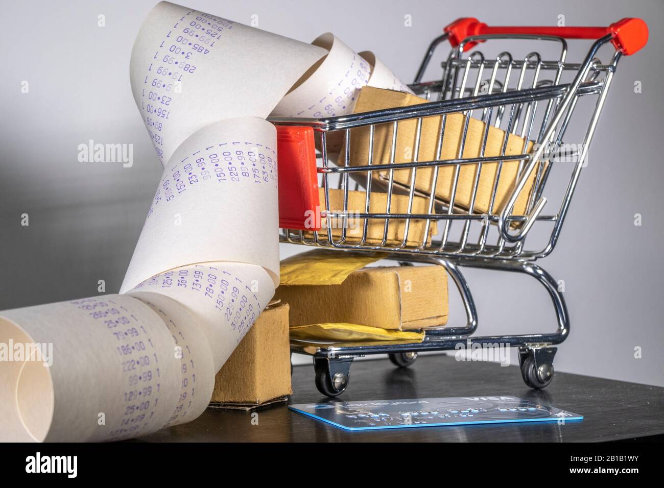 Concetto di shopping: Un carrello modello pieno di pacchi, con un lungo rotolo di spesa che fuoriesce, e una carta di credito / debito. Foto Stock