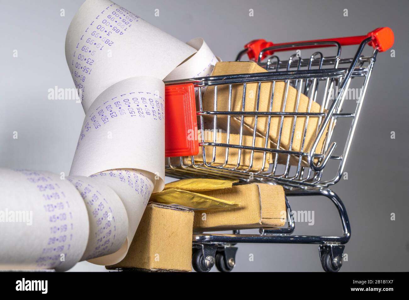 Concetto di shopping: Un carrello modello di shopping pieno di pacchi, con un lungo rotolo di spesa dettagliata che fuoriesce. Foto Stock