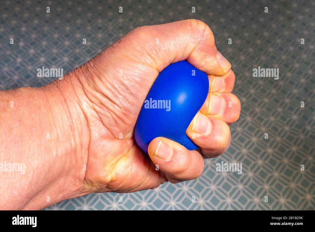 Mano di un uomo che tiene e stringe una palla morbida e blu. Foto Stock