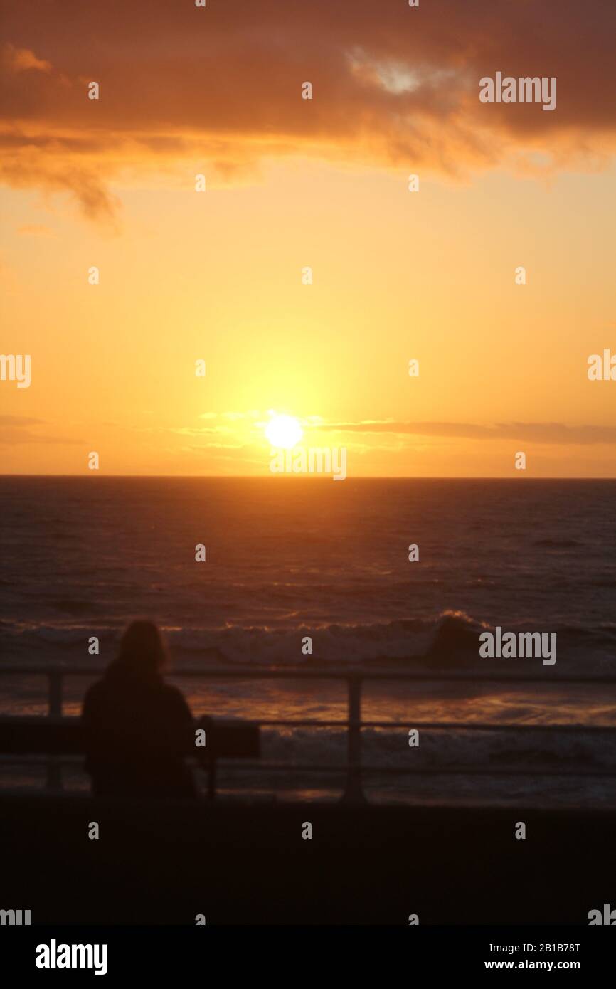 Aberystwyth Ceredigion Wales UK Weather 24th Febuary 2020 : Dopo una fredda giornata di vento con forte pioggia, la serata è tranquilla e un glorioso tramonto è visto da escursionisti lungo il lungomare di Aberystwyth sulla costa occidentale del Galles. Credito: Mike davies/Alamy Live News Foto Stock