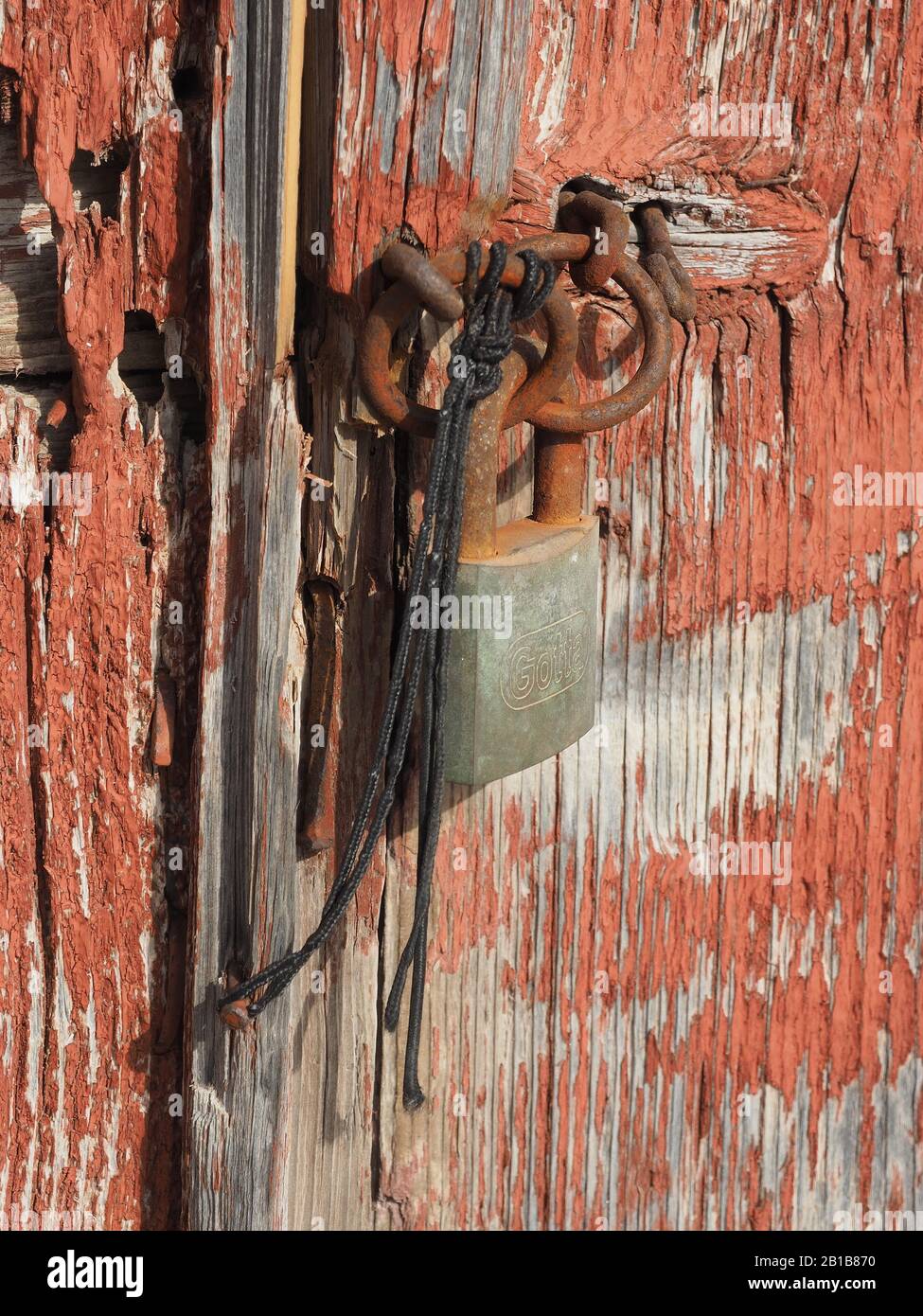 Vecchia porta di legno con vernice sfaldante e fissata con una serratura arrugginita e una lunghezza di spago in Kythira, Grecia. Foto Stock