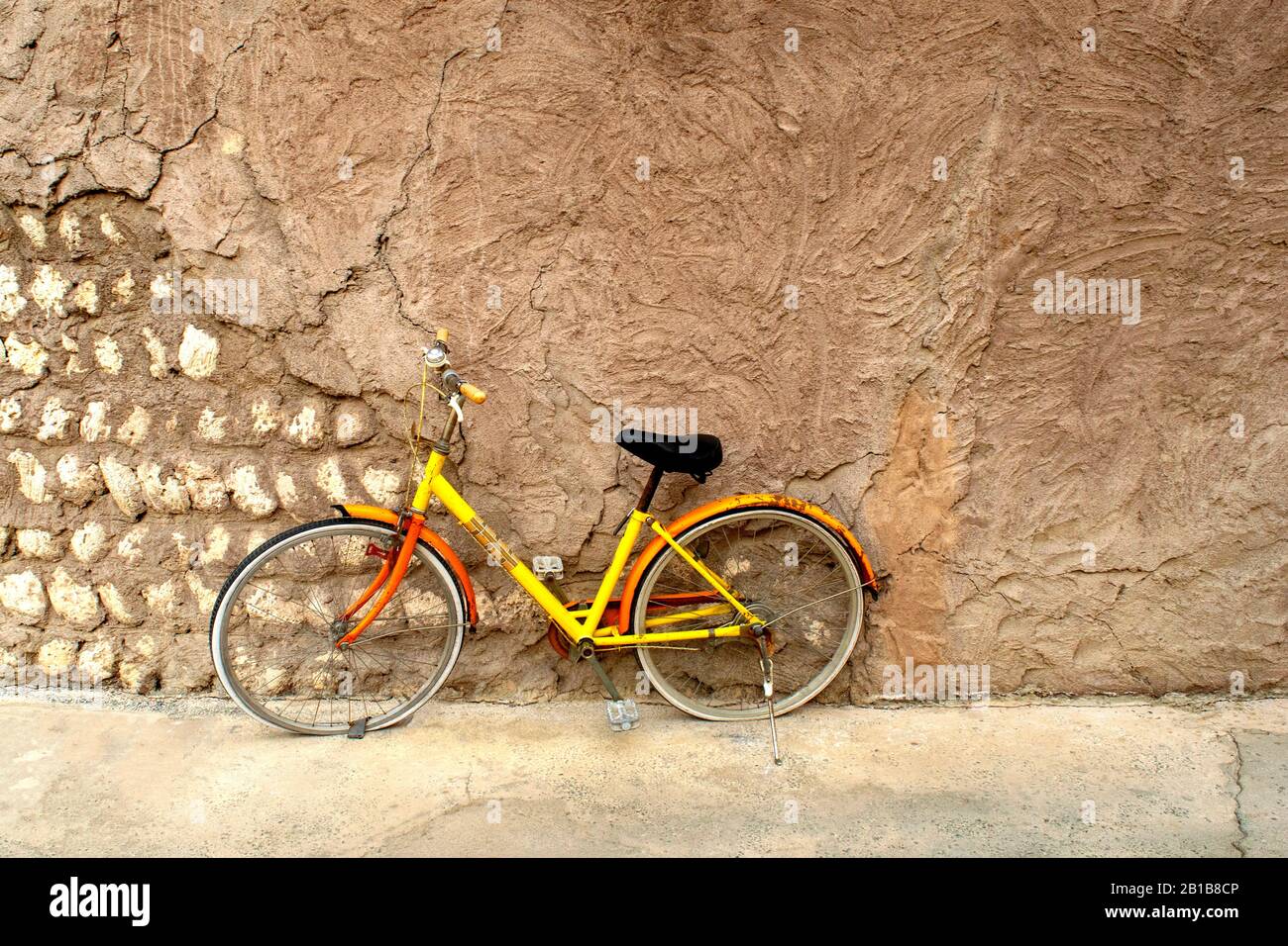 Colorata bici gialla brillante parcheggiata contro il muro d'epoca. Solitario singolo da solo una bicicletta abbandonata su una strada. Foto Stock