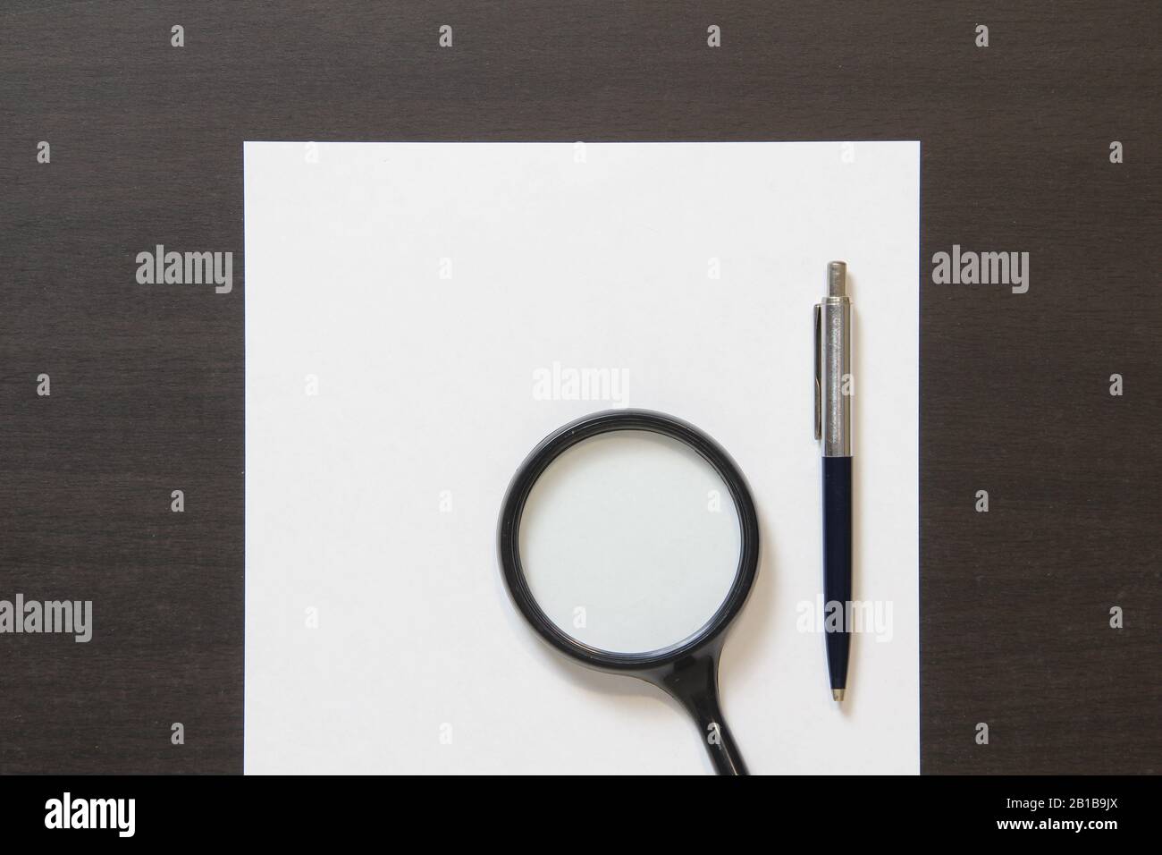 Modello di carta bianca con penna e lente di ingrandimento su sfondo di legno di colore wenge scuro. Concetto di business plan, ricerca, rilevamento e risoluzione dei problemi. Stock foto con spazio vuoto per il testo. Foto Stock