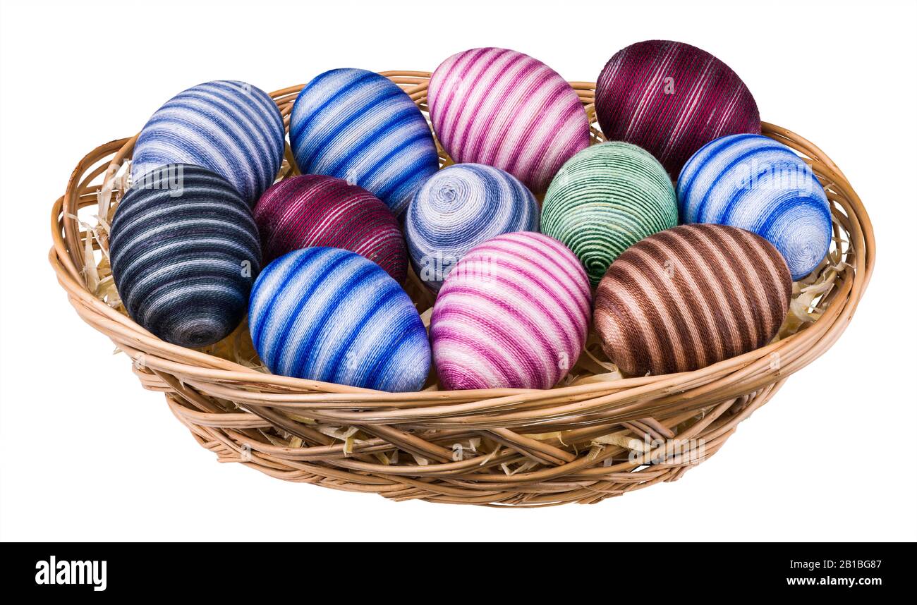 Uova di Pasqua a righe decorate a mano in cesto di vimini isolato su sfondo bianco. Gusci d'uovo vuoti colorati avvolti da filo di cucitura di cotone sottile incollato. Foto Stock