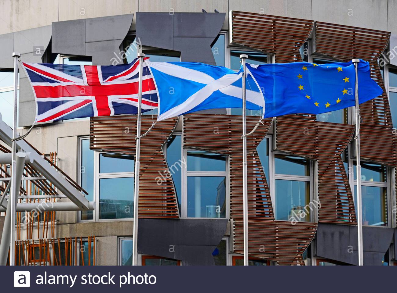 Le bandiere dell'Unione Jack, Saltire e dell'Unione europea al di fuori del parlamento scozzese si sono estese completamente con un vento forte Foto Stock
