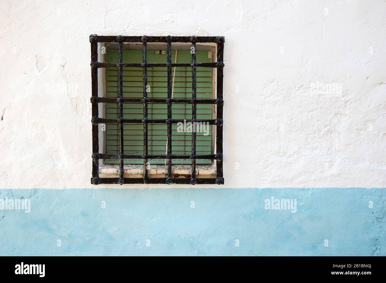 Antichi bar in ferro battuto sulla finestra della strada e serranda verde su un muro azzurro e bianco Foto Stock