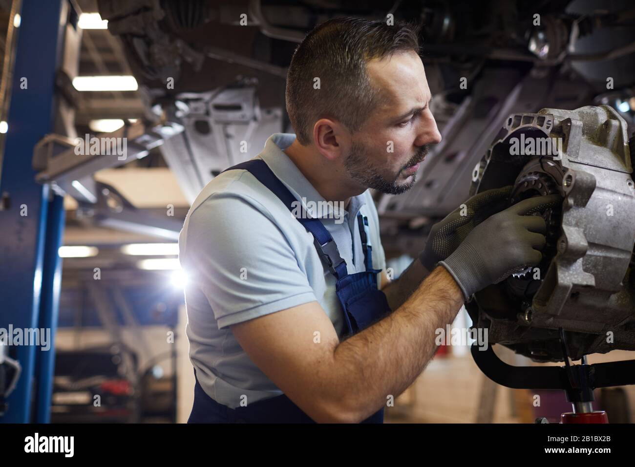 Vista laterale ritratto di meccanico di automobile con bearded che ripara il cambio nell'officina automatica, spazio di copia Foto Stock