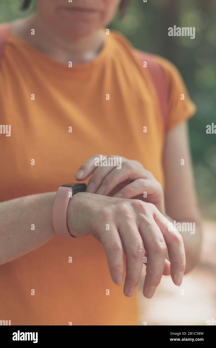 Donna escursionista che utilizza un braccialetto smart fitness tracker durante il trekking in natura. Primo piano di mani femminili con orologio fitness, fuoco selettivo. Foto Stock