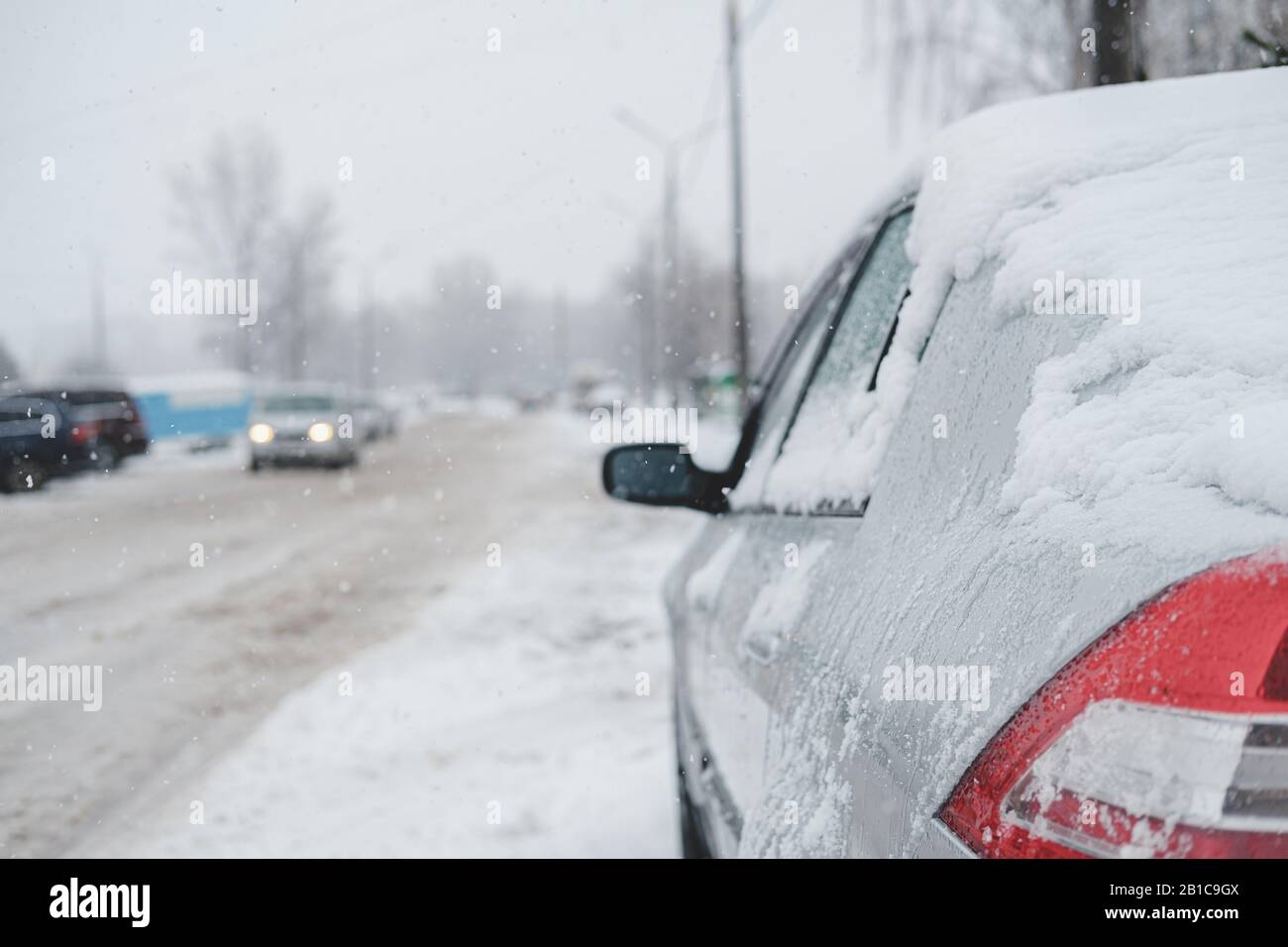 Un veicolo coperto di neve sulla strada. Traffico lento nella tempesta invernale, strada piena di neve bagnata Foto Stock
