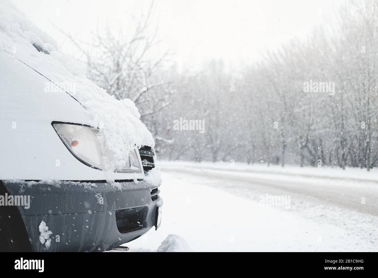 La parte anteriore di un'auto coperta di neve. Il veicolo si trova sulla strada innevata in condizioni climatiche tempestose Foto Stock