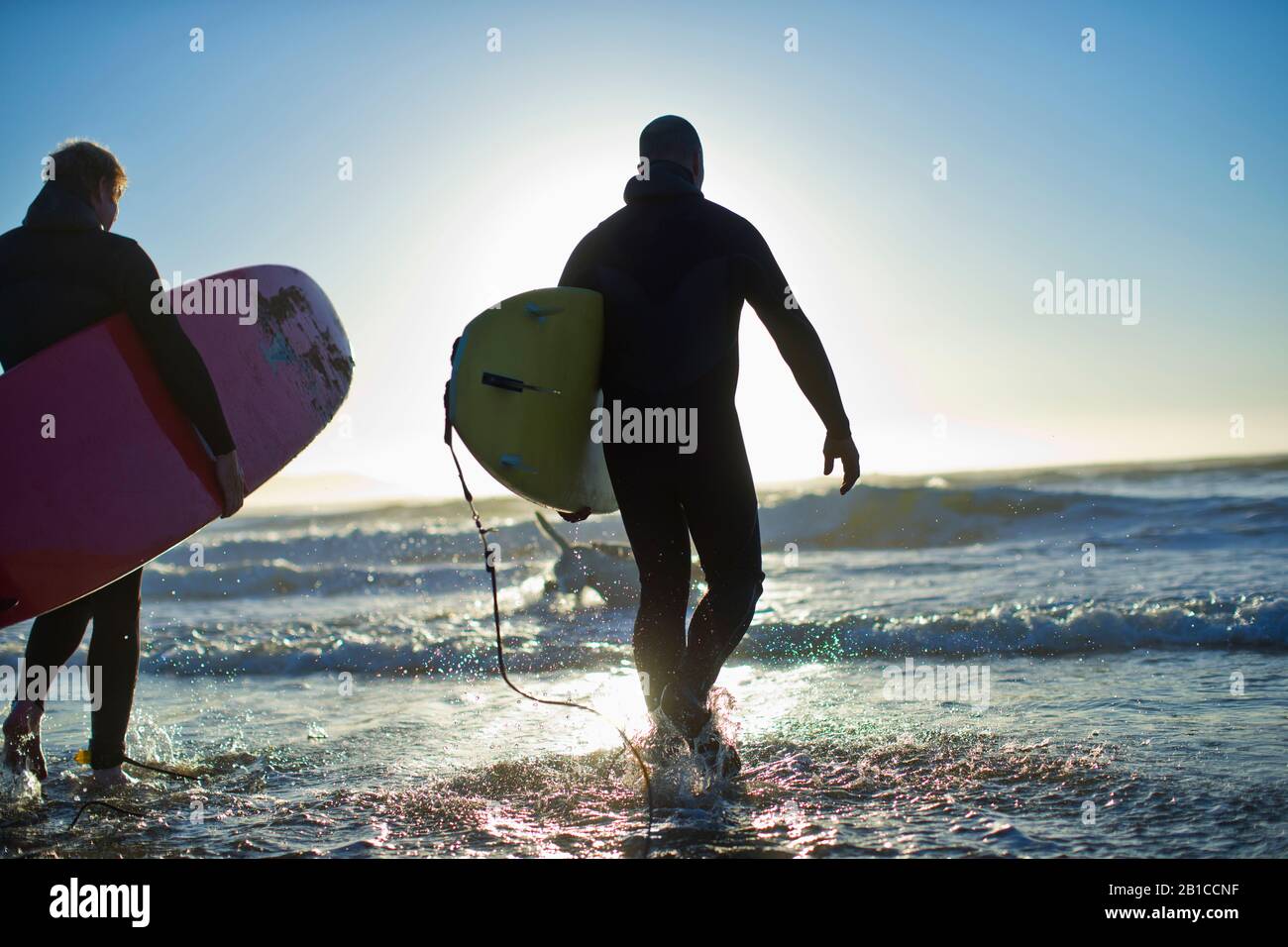 Due uomini adulti medi che camminano nell'oceano mentre tengono tavole da surf. Foto Stock