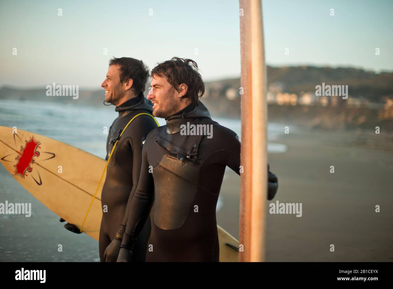 Amici sorridenti in piedi con tavole da surf su una spiaggia. Foto Stock