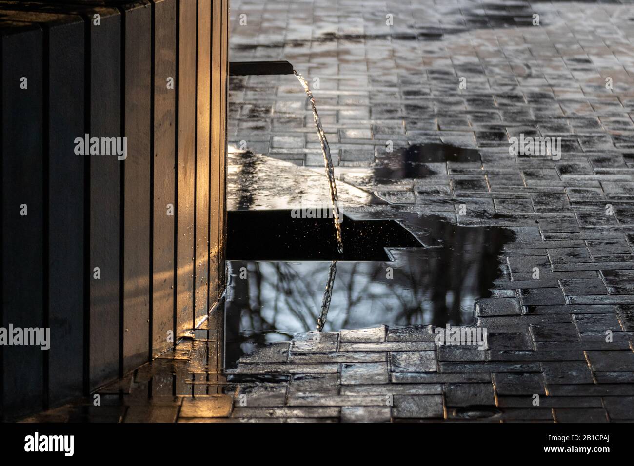 Acqua potabile chiara di sorgente sparking in luce del tramonto e correre da nero scuro fonte di acqua di pietra. Acqua di pulizia naturale. Foto Stock