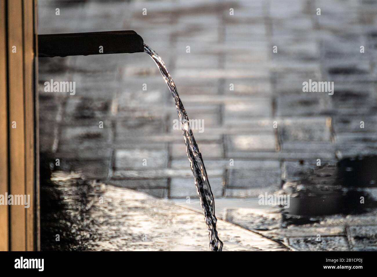 Acqua potabile chiara di sorgente sparking in luce del tramonto e correre da nero scuro fonte di acqua di pietra. Acqua di pulizia naturale. Foto Stock