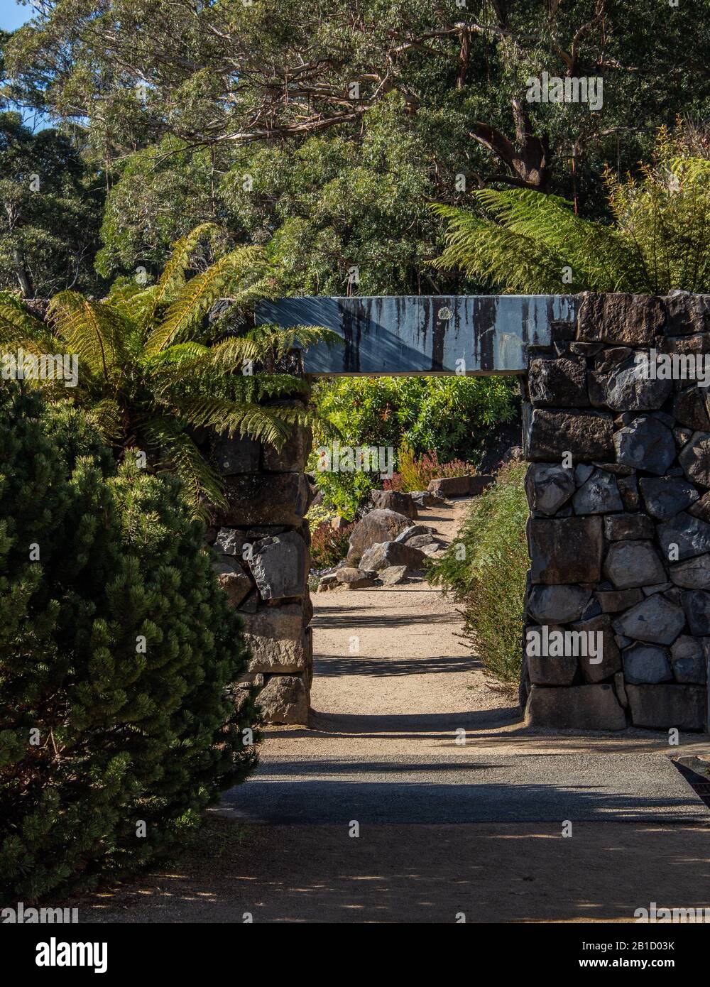 Sentiero da giardino con pareti in pietra, arco porta lungo passerella in pietra circondata da alberi Foto Stock