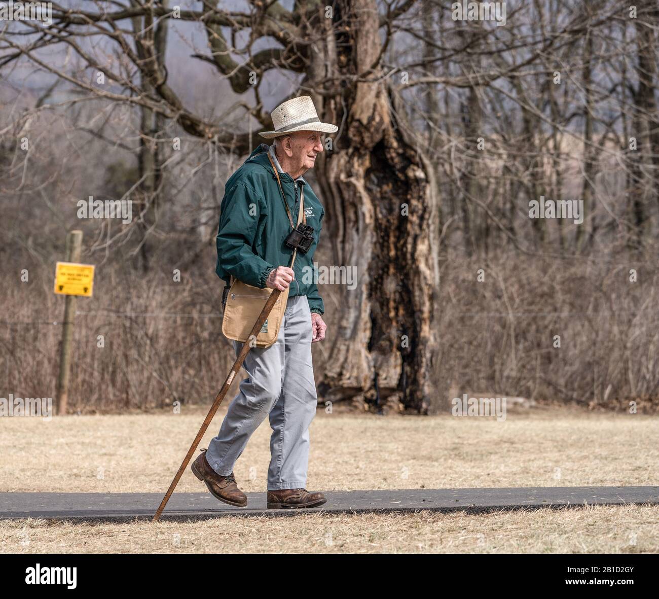 Lancaster County, Pennsylvania USA: 24 febbraio 2020: Uomo anziano con bastone da passeggio che si gode una calda giornata invernale mentre fa una passeggiata nel parco. Foto Stock