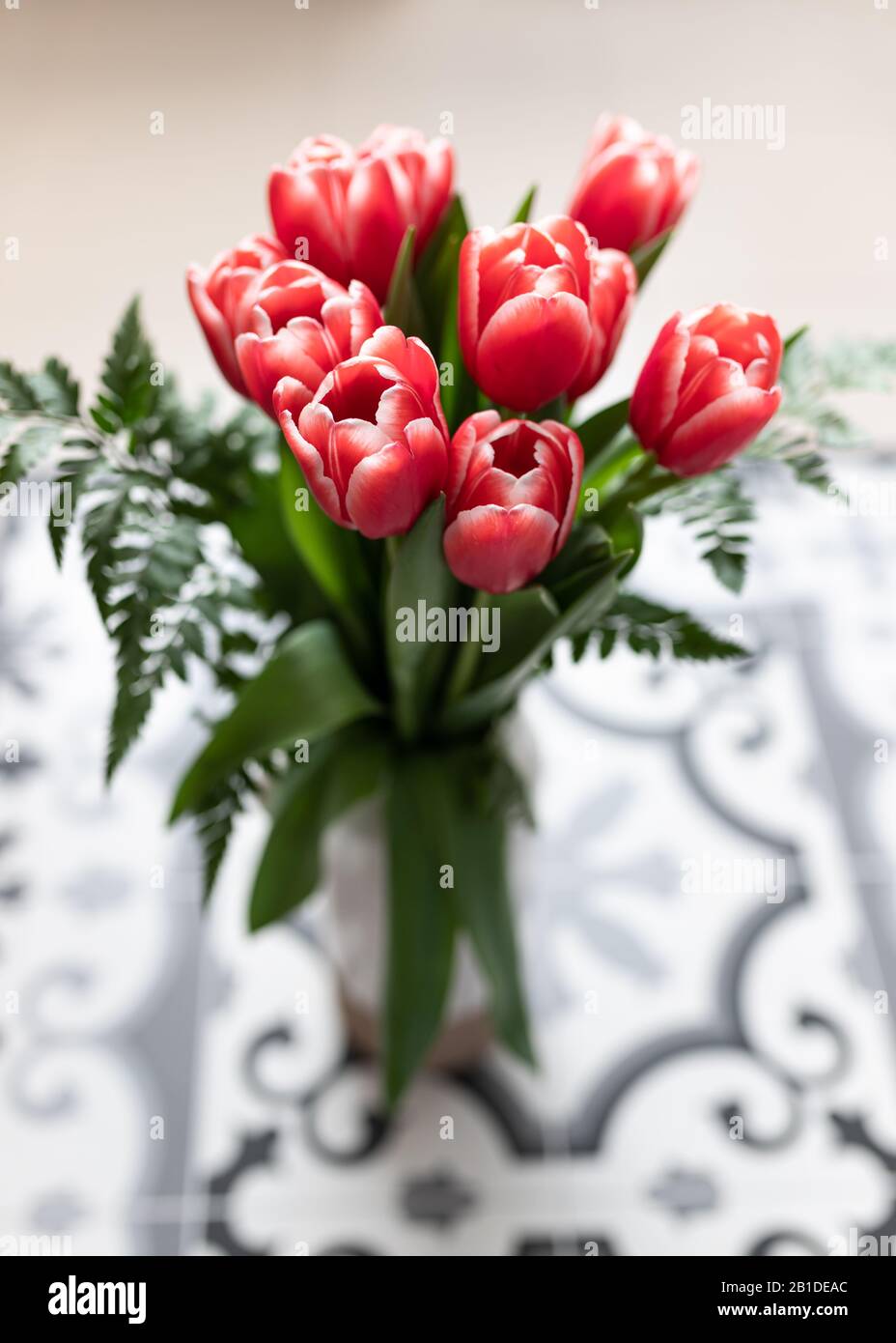 Vista closeup di un bouquet di tulipano rosso in un vaso trasparente su un pavimento idraulico. Foto Stock