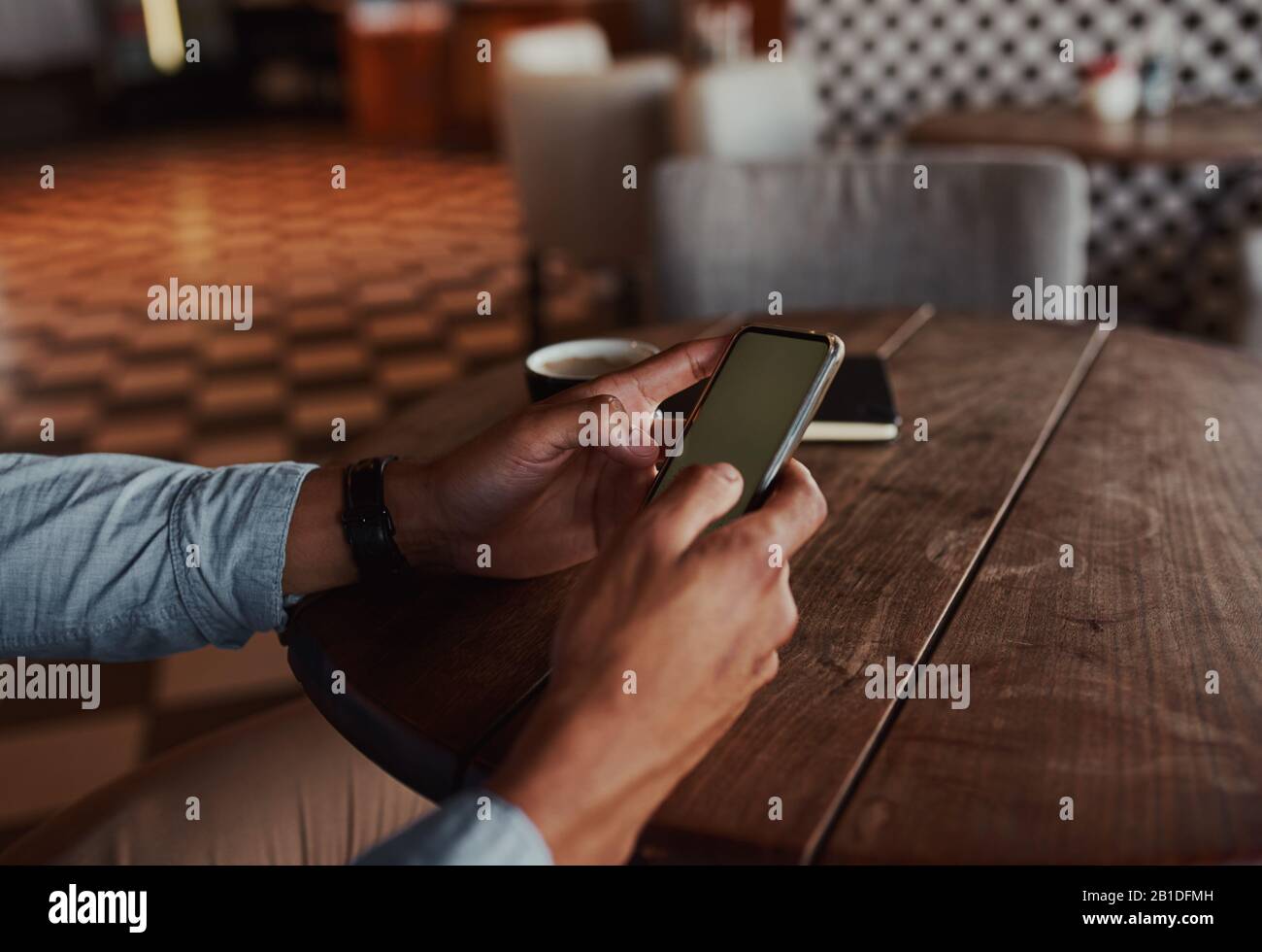 Chiudiere le mani dell'uomo usando lo smartphone mentre si siede nel caffè bevendo il caffè usando il touchscreen Foto Stock