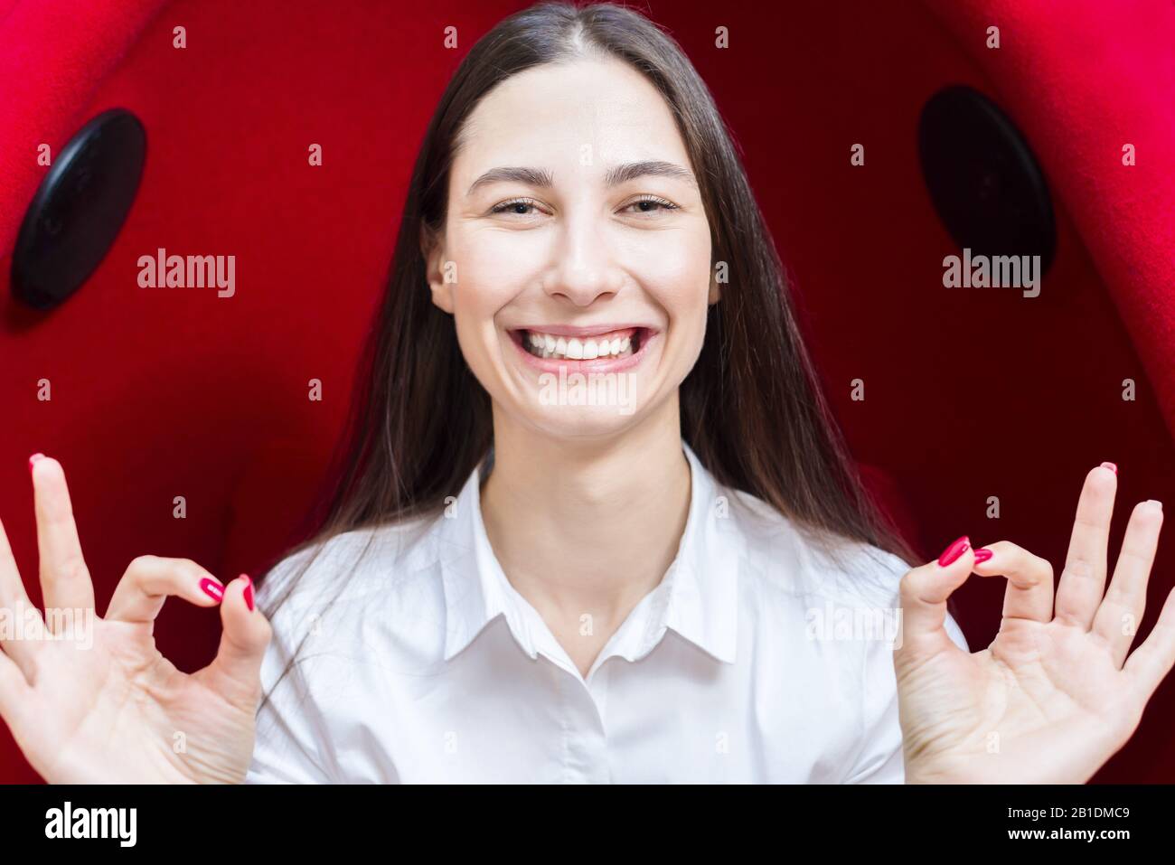 felice giovane ragazza sorridente. donna mostra gesto tutto va bene. sfondo rosso Foto Stock