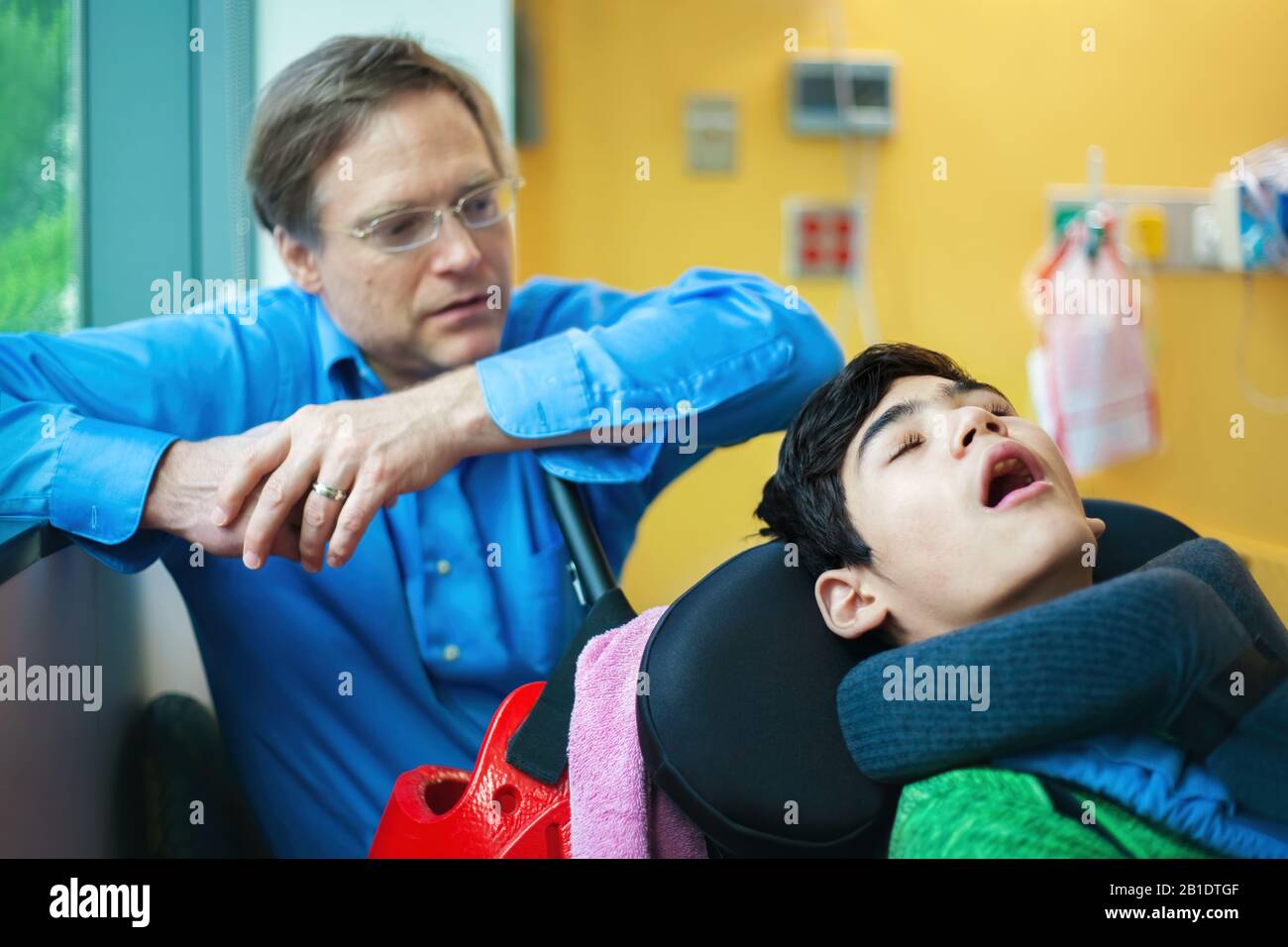 Preoccupato il padre che guarda sopra il figlio disabile addormentato in sedia a rotelle all'ospedale Foto Stock