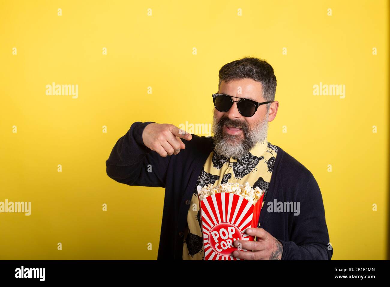 Uomo con barba bianca e occhiali da sole su sfondo giallo isolato che tiene  un grande secchio di popcorn mentre punta in avanti Foto stock - Alamy