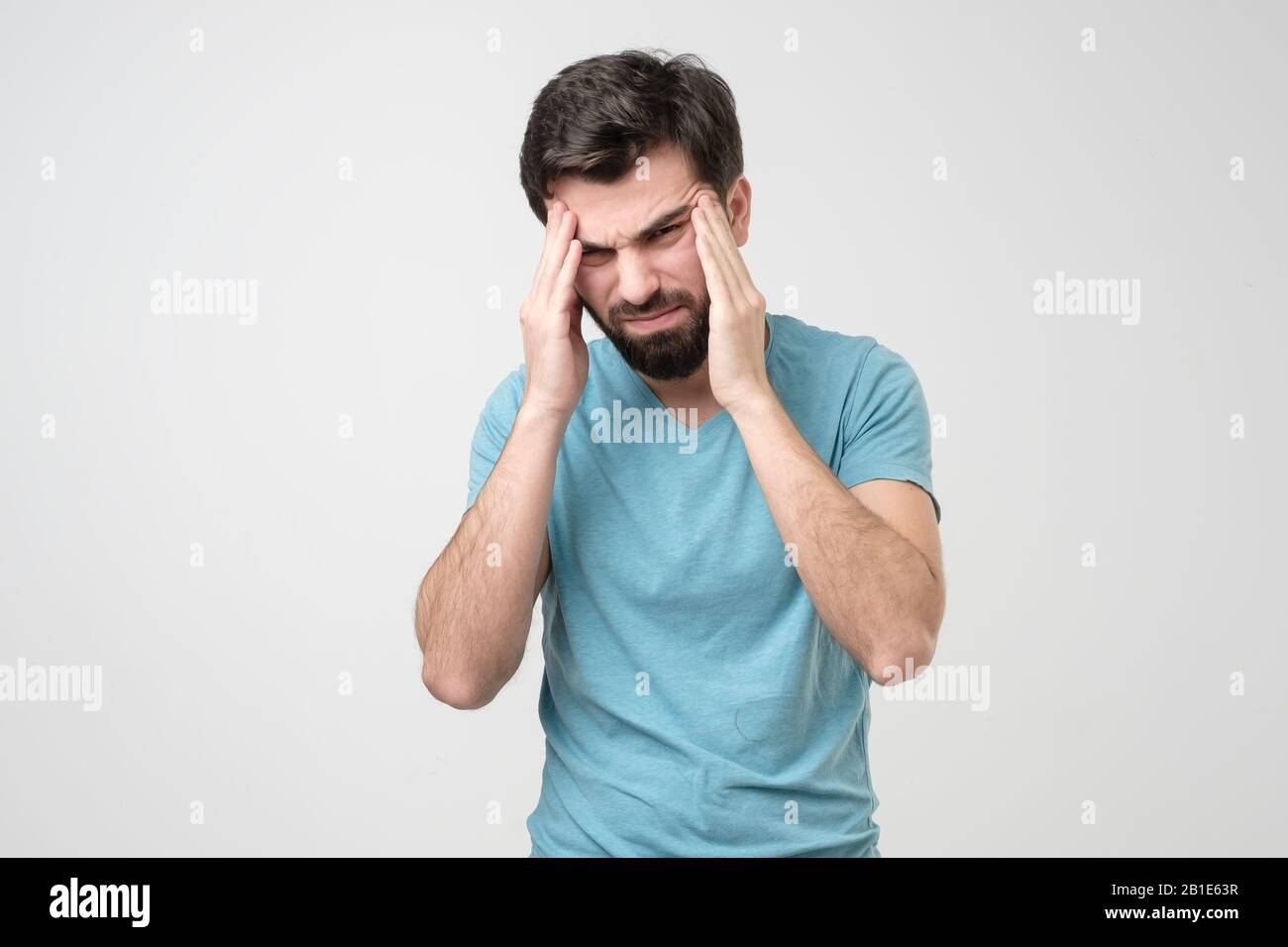 Un giovane preoccupato che soffre di mal di testa tenendo le mani sui templi. Emozione facciale negativa. Foto Stock Un giovane preoccupato che soffre di mal di testa tenendo le mani sui templi. Emozione facciale negativa. Foto Stock