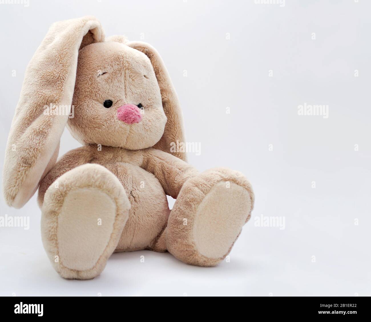 un bambino carino peloso coniglio giocattolo seduto su uno sfondo luminoso Foto Stock