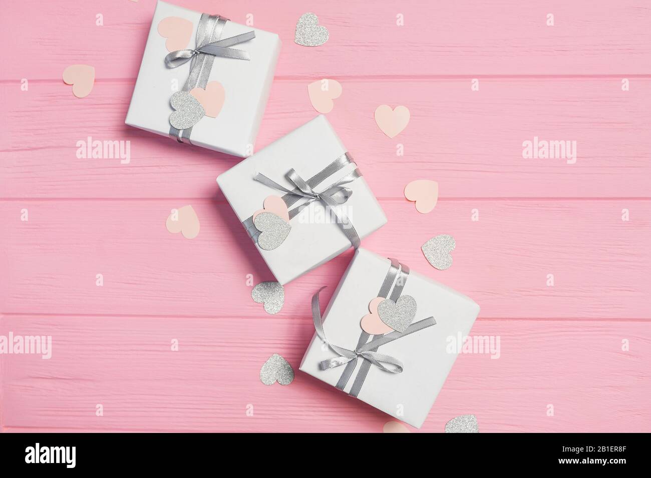 Scatole bianche regalo con nastro in raso argento e confetti in forma di cuore su sfondo rosa amore. Mock up il giorno delle donne, San Valentino, buon compleanno Foto Stock