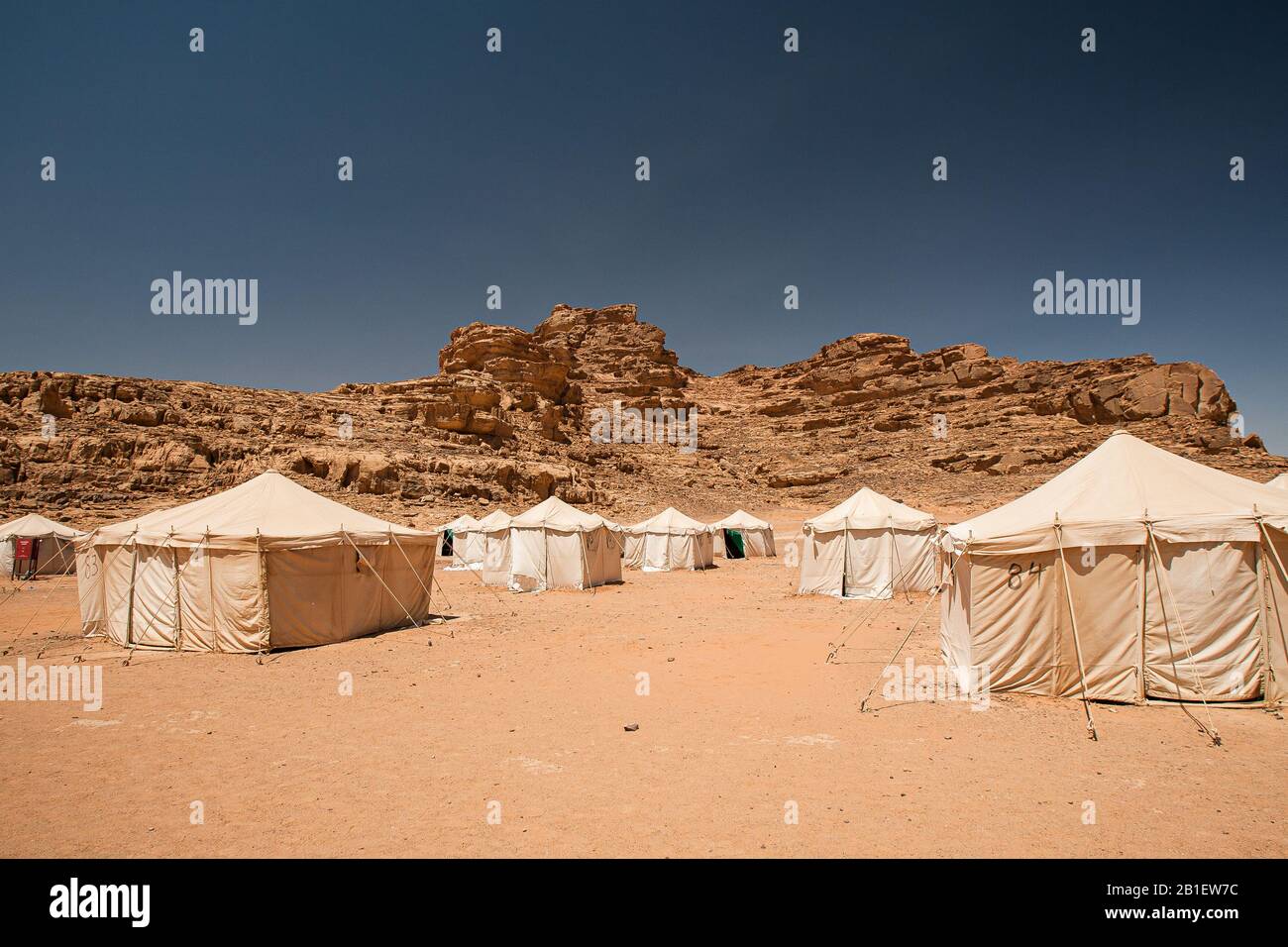 File di tende bianche nel deserto sotto le colline rocciose nel campo di Jabal Rum a Wadi Rum, Giordania. Foto Stock