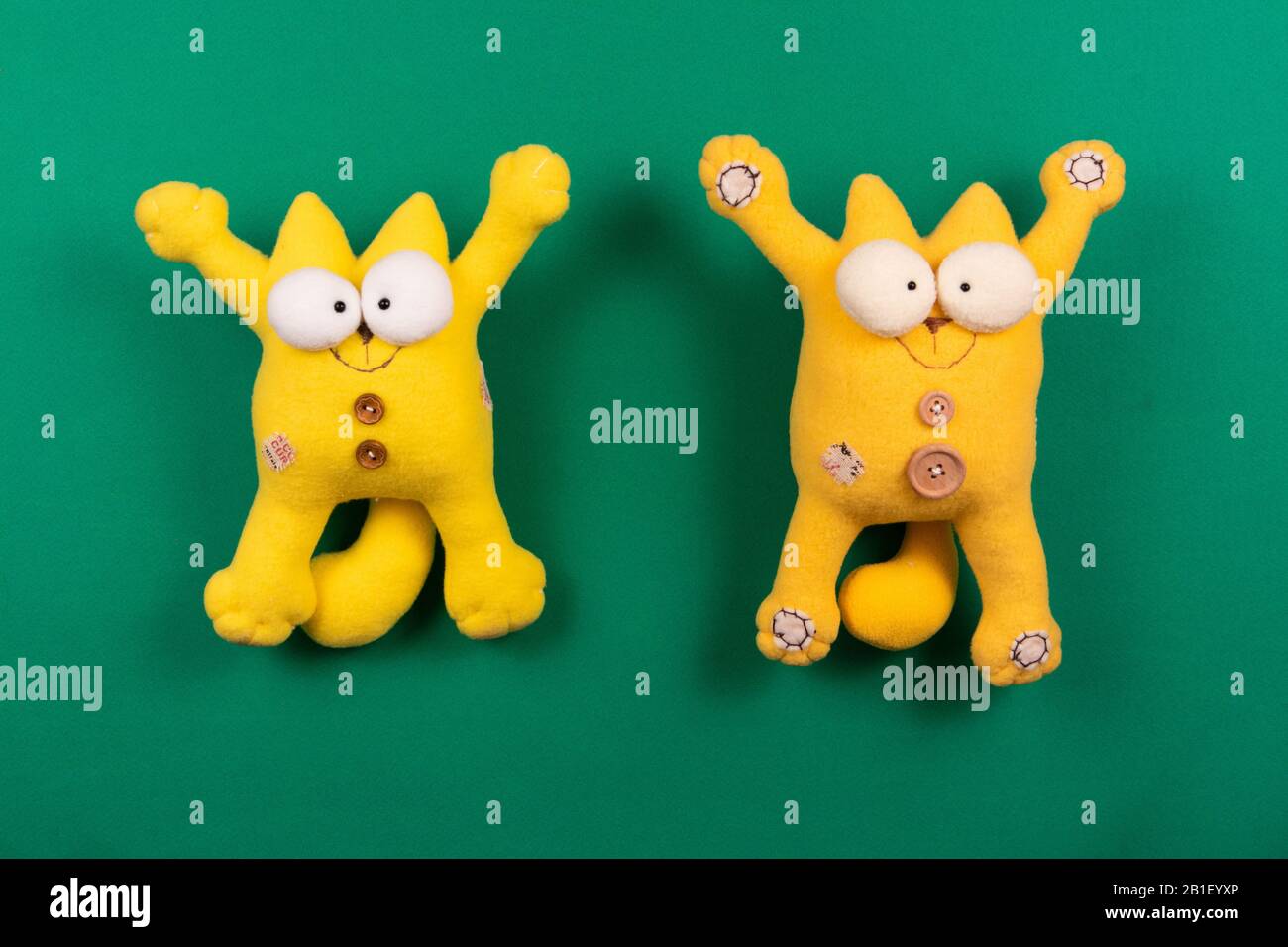 Due simpatici gatti sorridenti gialli con zampe aperte sullo sfondo verde, giocattoli soffici firmati Foto Stock